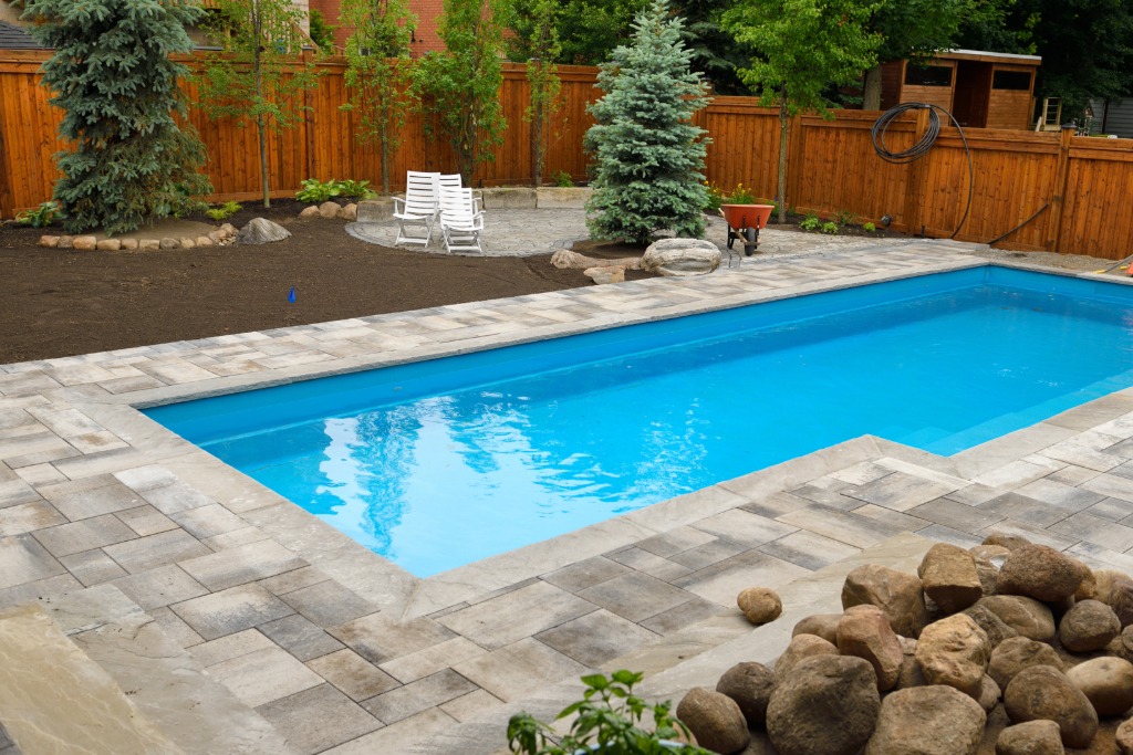 Newly built backyard pool with stone paver patio and landscaping in progress.