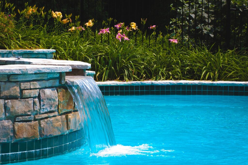 Stone waterfall feature flowing into a clear blue backyard swimming pool.