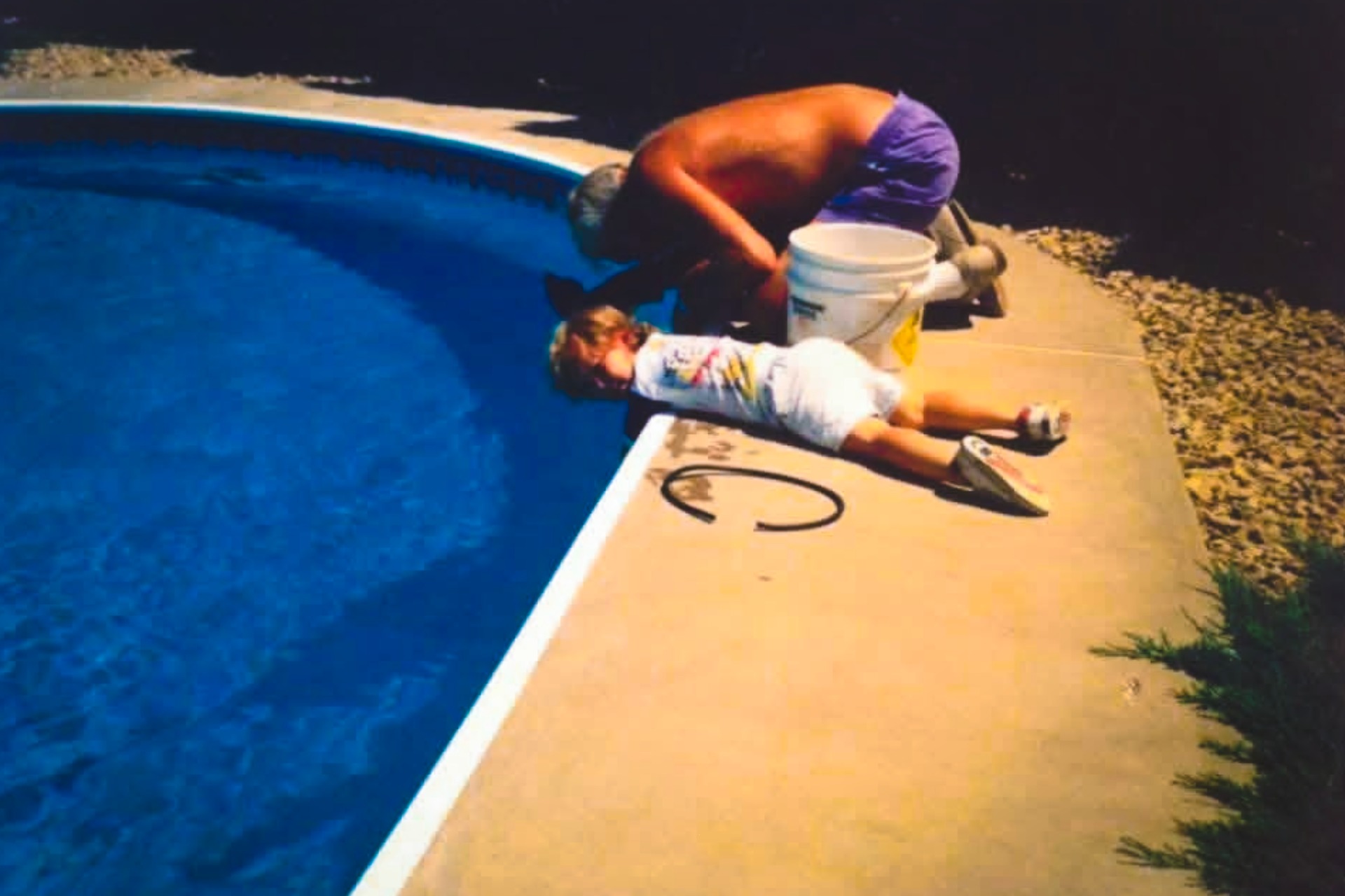 Young boy and his grandfather working together by a swimming pool, symbolizing the family legacy behind the pool company.