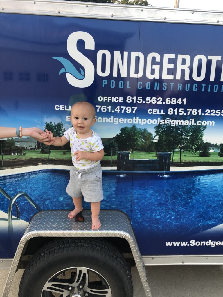 A child standing on the wheel of a work truck, highlighting the size and scale of the vehicle in an outdoor setting.